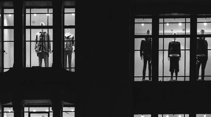 A black-and-white photograph of illuminated store window displays featuring clothing mannequins at night.
