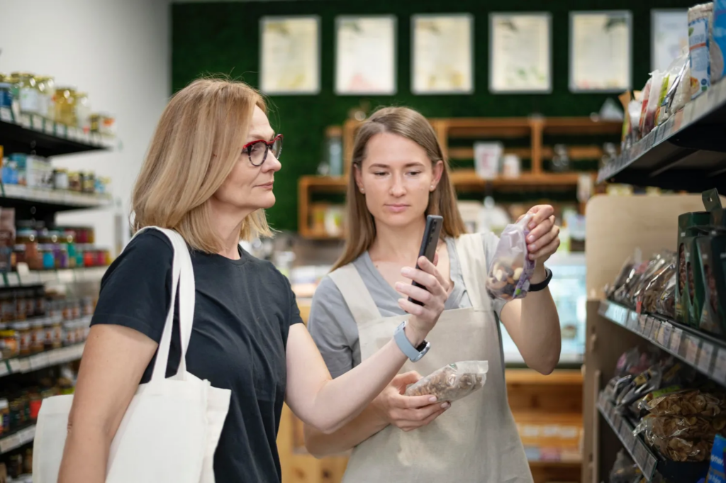 A retail worker assisting a customer by scanning a product with a smartphone in a grocery store.